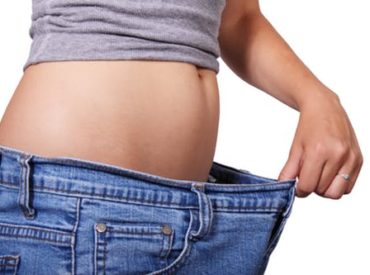 Woman holding out waist of jeans to show her belly and weight loss through health coaching